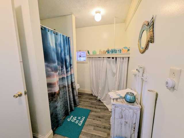 bathroom with a shower with curtain, toilet, a textured ceiling, wood finished floors, and baseboards