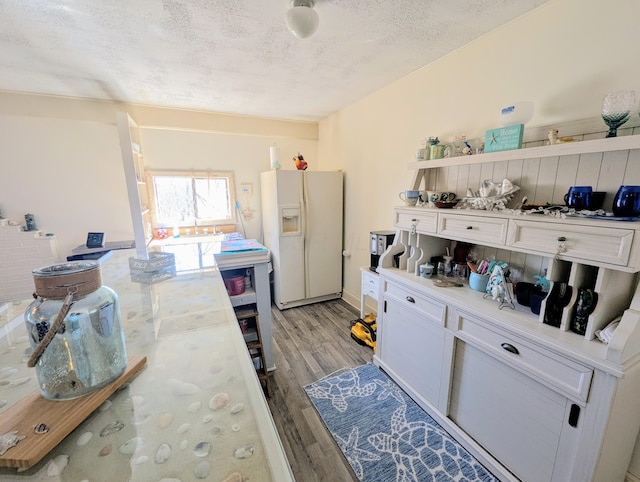kitchen featuring light wood-style flooring, open shelves, a textured ceiling, white refrigerator with ice dispenser, and light countertops