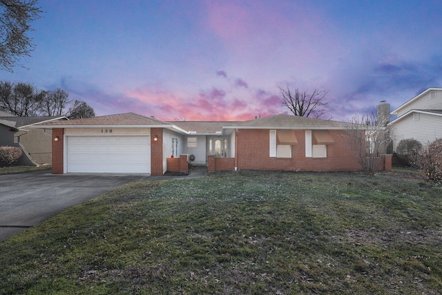 single story home with a garage, a front lawn, brick siding, and driveway