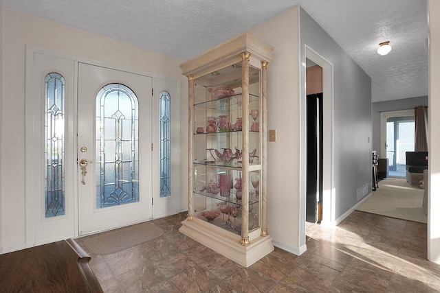 foyer with visible vents, a textured ceiling, and baseboards