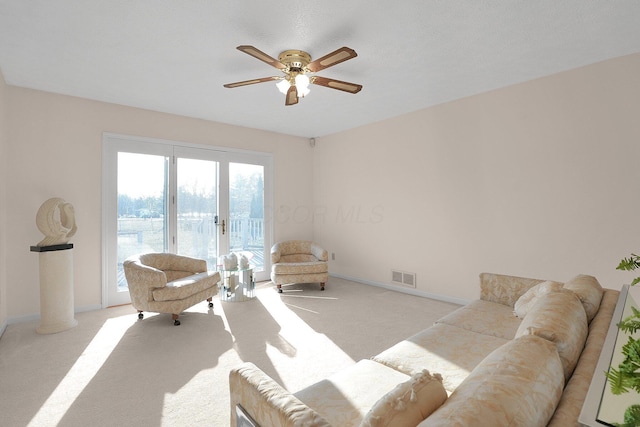 living area with visible vents, light carpet, baseboards, and ceiling fan