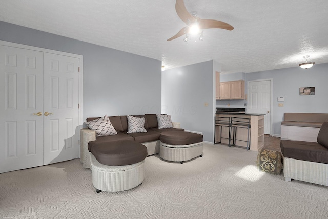 living area featuring baseboards, a ceiling fan, light colored carpet, and a textured ceiling