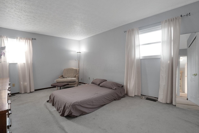 bedroom with a textured ceiling, multiple windows, visible vents, and light carpet