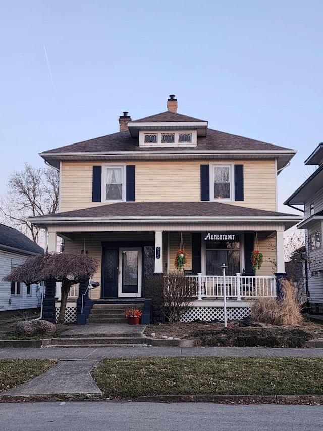 traditional style home with roof with shingles, covered porch, and a chimney