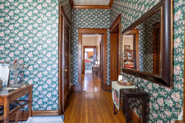 corridor with wood finished floors, ornamental molding, and wallpapered walls