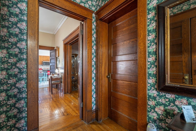 hallway featuring wood finished floors, crown molding, and wallpapered walls
