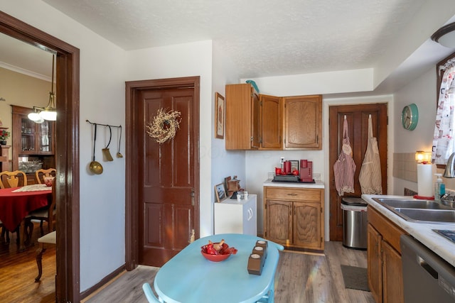 kitchen with light wood finished floors, a sink, light countertops, stainless steel dishwasher, and brown cabinets