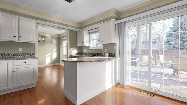 kitchen featuring visible vents, baseboards, a peninsula, wood finished floors, and white cabinets