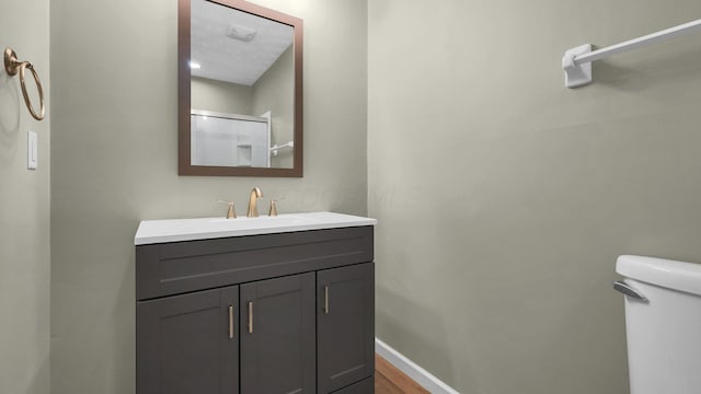 bathroom with toilet, a shower with door, wood finished floors, baseboards, and vanity