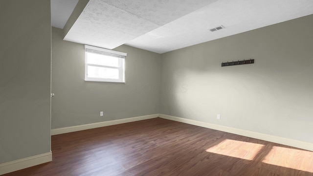 empty room featuring visible vents, baseboards, a textured ceiling, and wood finished floors