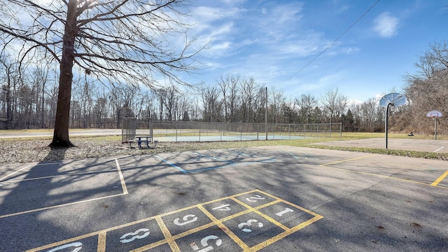 view of community with a tennis court, community basketball court, fence, and uncovered parking