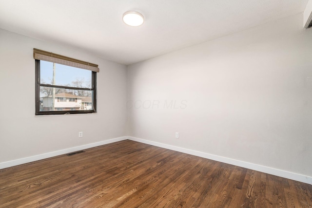 unfurnished room with visible vents, baseboards, and dark wood-style flooring