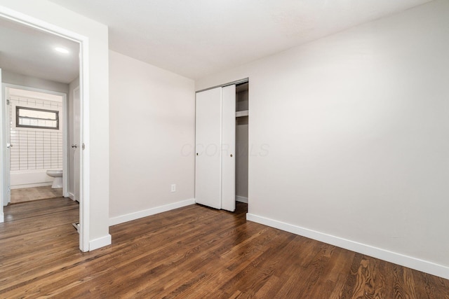 unfurnished bedroom featuring dark wood-style floors, baseboards, and a closet