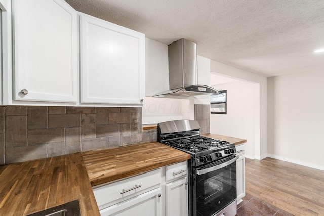 kitchen featuring backsplash, white cabinets, butcher block counters, wall chimney range hood, and stainless steel gas range