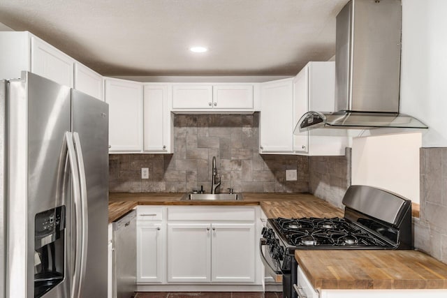 kitchen with butcher block countertops, a sink, stainless steel appliances, wall chimney exhaust hood, and white cabinets