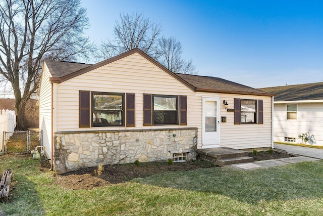 view of front of home featuring stone siding, roof with shingles, a front yard, and fence