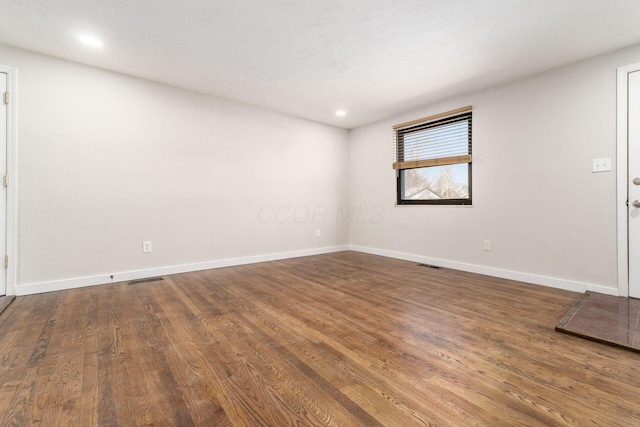 empty room featuring visible vents, baseboards, and wood finished floors