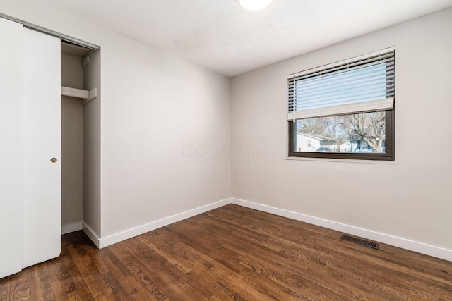 unfurnished bedroom featuring a closet, visible vents, dark wood-type flooring, and baseboards