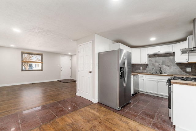 kitchen with dark wood-style floors, a sink, stainless steel appliances, white cabinets, and backsplash