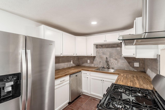 kitchen with tasteful backsplash, exhaust hood, stainless steel appliances, wood counters, and a sink