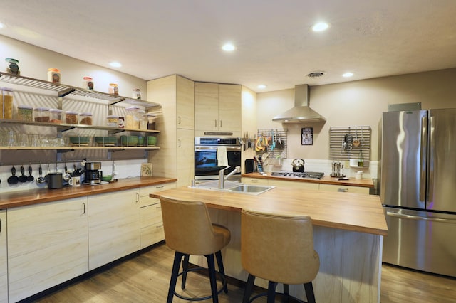 kitchen featuring visible vents, a sink, appliances with stainless steel finishes, butcher block counters, and wall chimney range hood