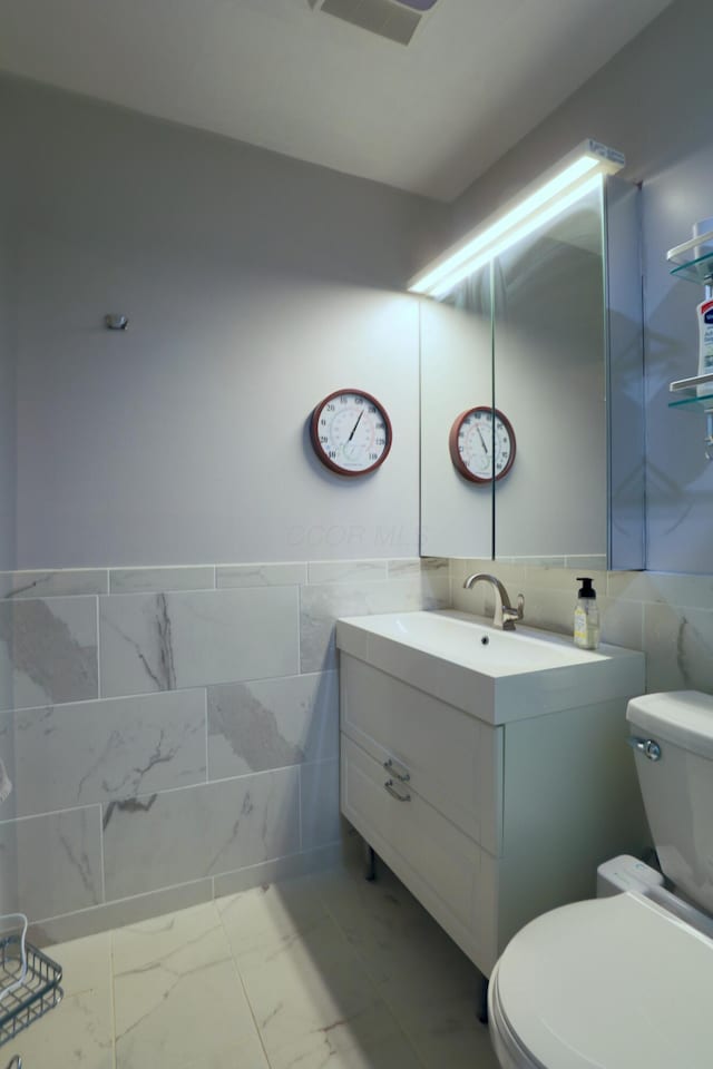 half bathroom featuring tile walls, toilet, marble finish floor, and vanity