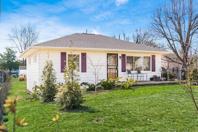 view of front facade with roof with shingles, a front yard, and fence