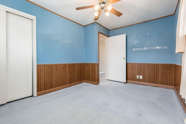 spare room with visible vents, ornamental molding, a ceiling fan, wood walls, and wainscoting