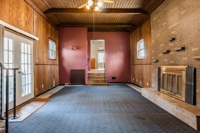 unfurnished living room with stairway, beam ceiling, ceiling fan, wooden ceiling, and a brick fireplace