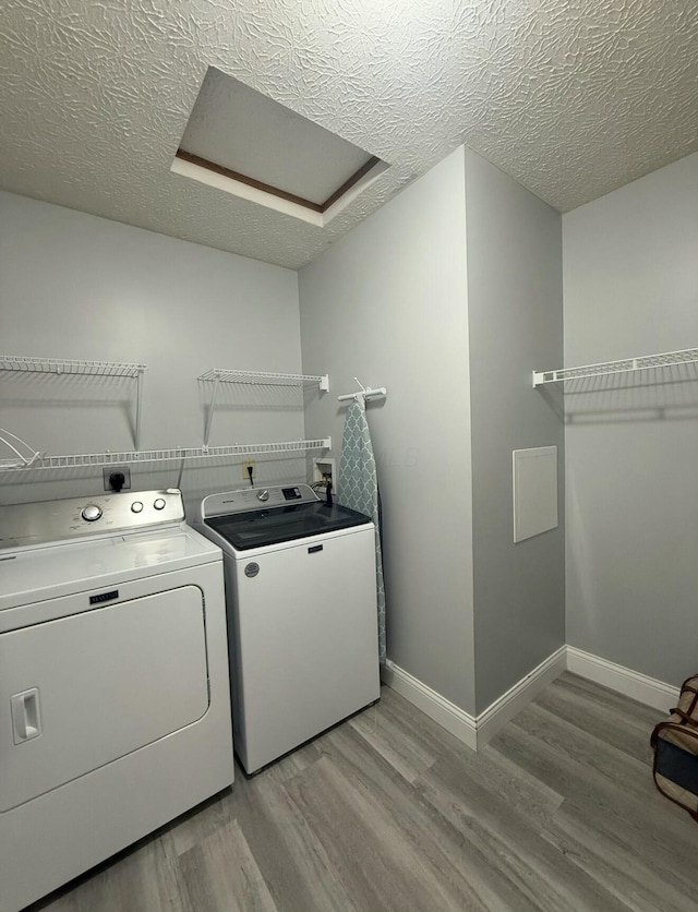 clothes washing area with independent washer and dryer, attic access, laundry area, a textured ceiling, and light wood-type flooring