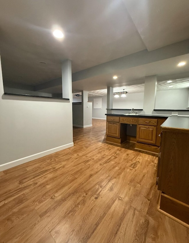 kitchen featuring light wood finished floors, dark countertops, baseboards, brown cabinetry, and a sink