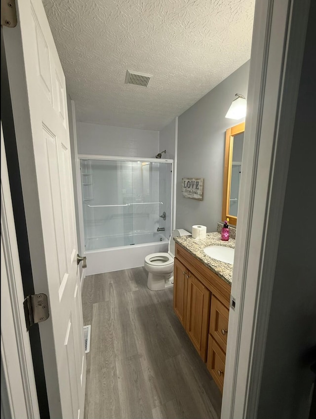 bathroom featuring visible vents, toilet, wood finished floors, shower / bath combination with glass door, and vanity