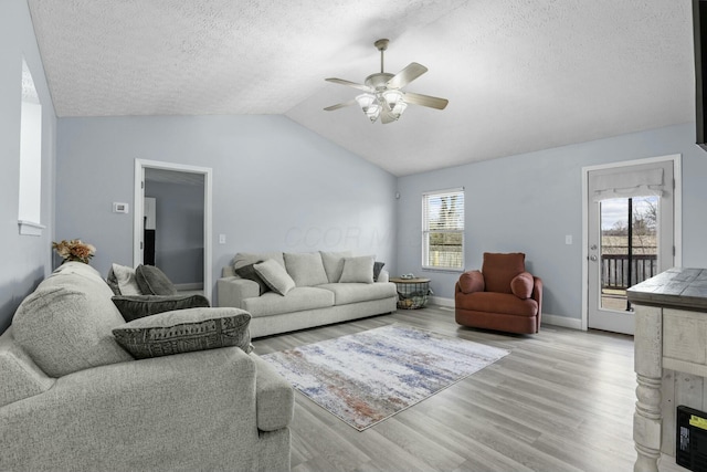 living area with light wood-style flooring, a ceiling fan, a textured ceiling, baseboards, and vaulted ceiling