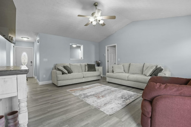 living area featuring a ceiling fan, a textured ceiling, wood finished floors, baseboards, and vaulted ceiling