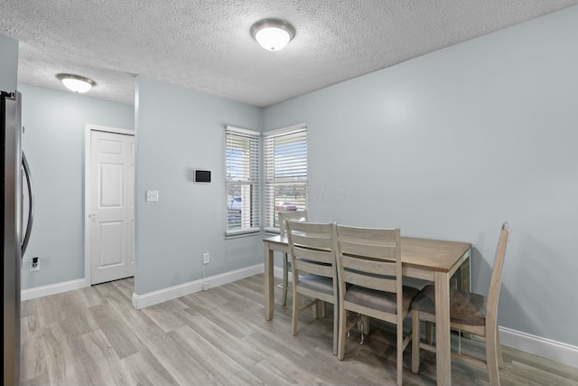 dining room with a textured ceiling, light wood-type flooring, and baseboards