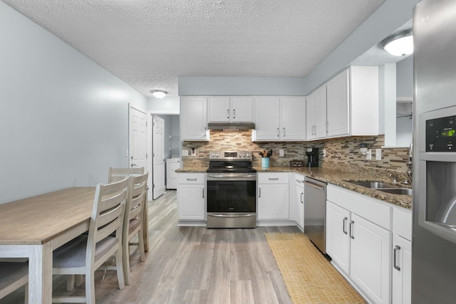 kitchen with under cabinet range hood, stainless steel appliances, light wood-style floors, and dark stone countertops