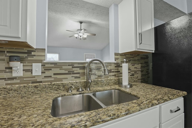 kitchen featuring light stone counters, white cabinetry, ceiling fan, and a sink