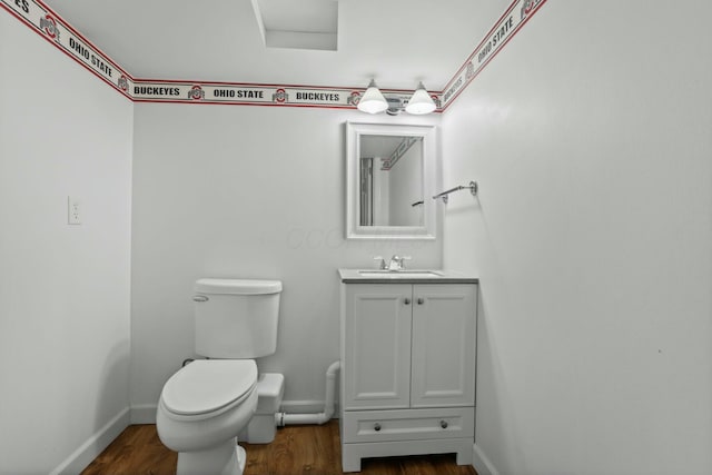 half bath with vanity, toilet, wood finished floors, and baseboards