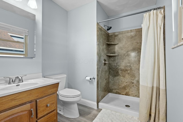 bathroom with baseboards, toilet, a tile shower, wood finished floors, and vanity