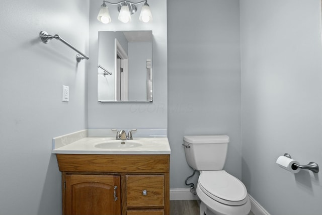 bathroom featuring toilet, vanity, baseboards, and wood finished floors