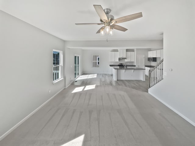 unfurnished living room with stairway, baseboards, and a ceiling fan