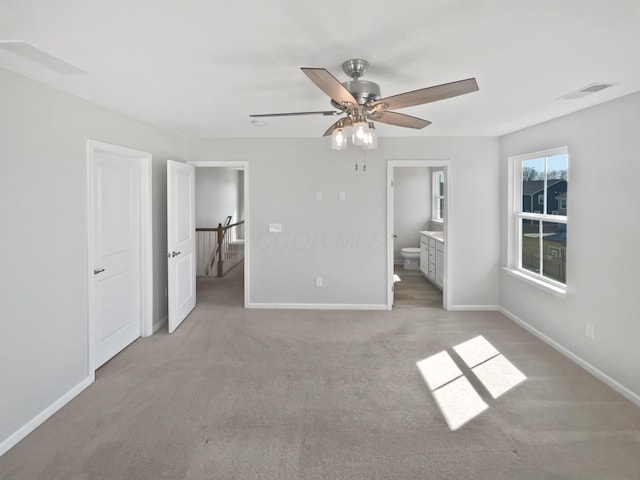 unfurnished bedroom featuring visible vents, connected bathroom, baseboards, ceiling fan, and light carpet