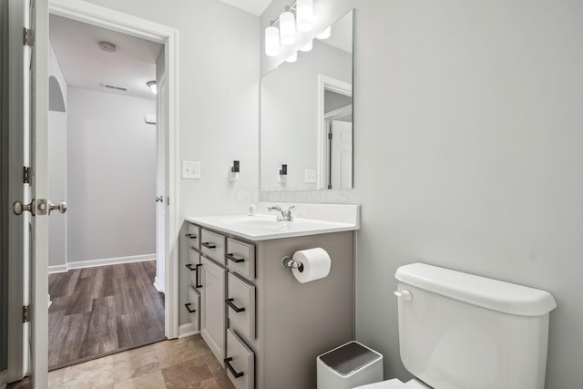 half bathroom with vanity, toilet, baseboards, and visible vents