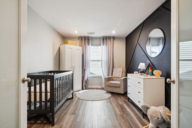 bedroom featuring visible vents, a crib, a textured ceiling, and wood finished floors