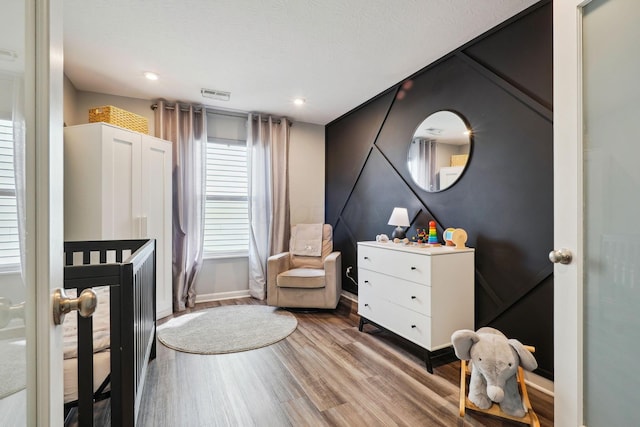 bedroom featuring visible vents, a crib, wood finished floors, recessed lighting, and baseboards