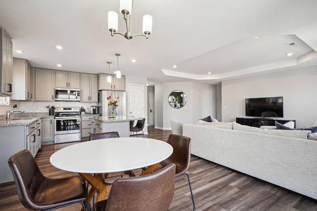 dining room featuring baseboards, a tray ceiling, recessed lighting, an inviting chandelier, and dark wood-style floors