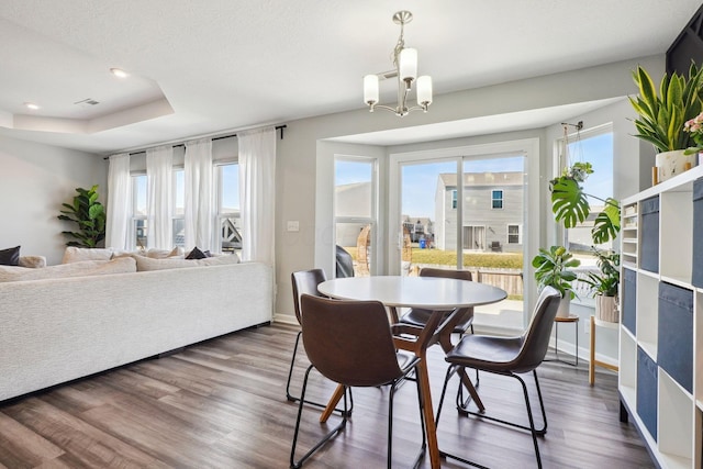 dining space featuring visible vents, dark wood-style floors, baseboards, a raised ceiling, and a chandelier