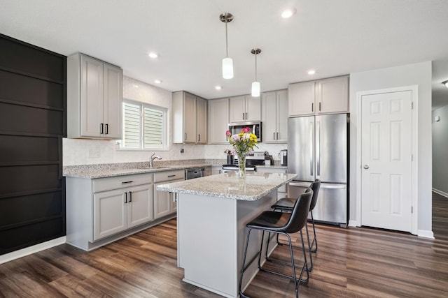 kitchen featuring light stone counters, a breakfast bar, dark wood-style flooring, gray cabinets, and appliances with stainless steel finishes