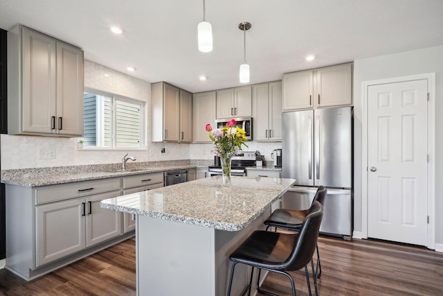 kitchen with a breakfast bar area, gray cabinets, dark wood-style flooring, stainless steel appliances, and a center island