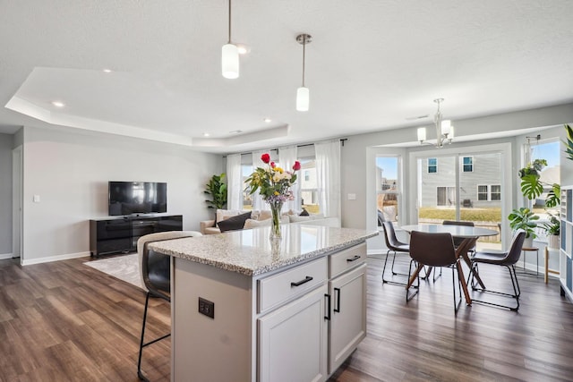 kitchen with pendant lighting, a tray ceiling, dark wood finished floors, a center island, and a chandelier